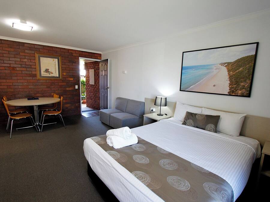Ein Hotelzimmer mit Bett, Schreibtisch, Sessel, Sofa und einem Strandbild.