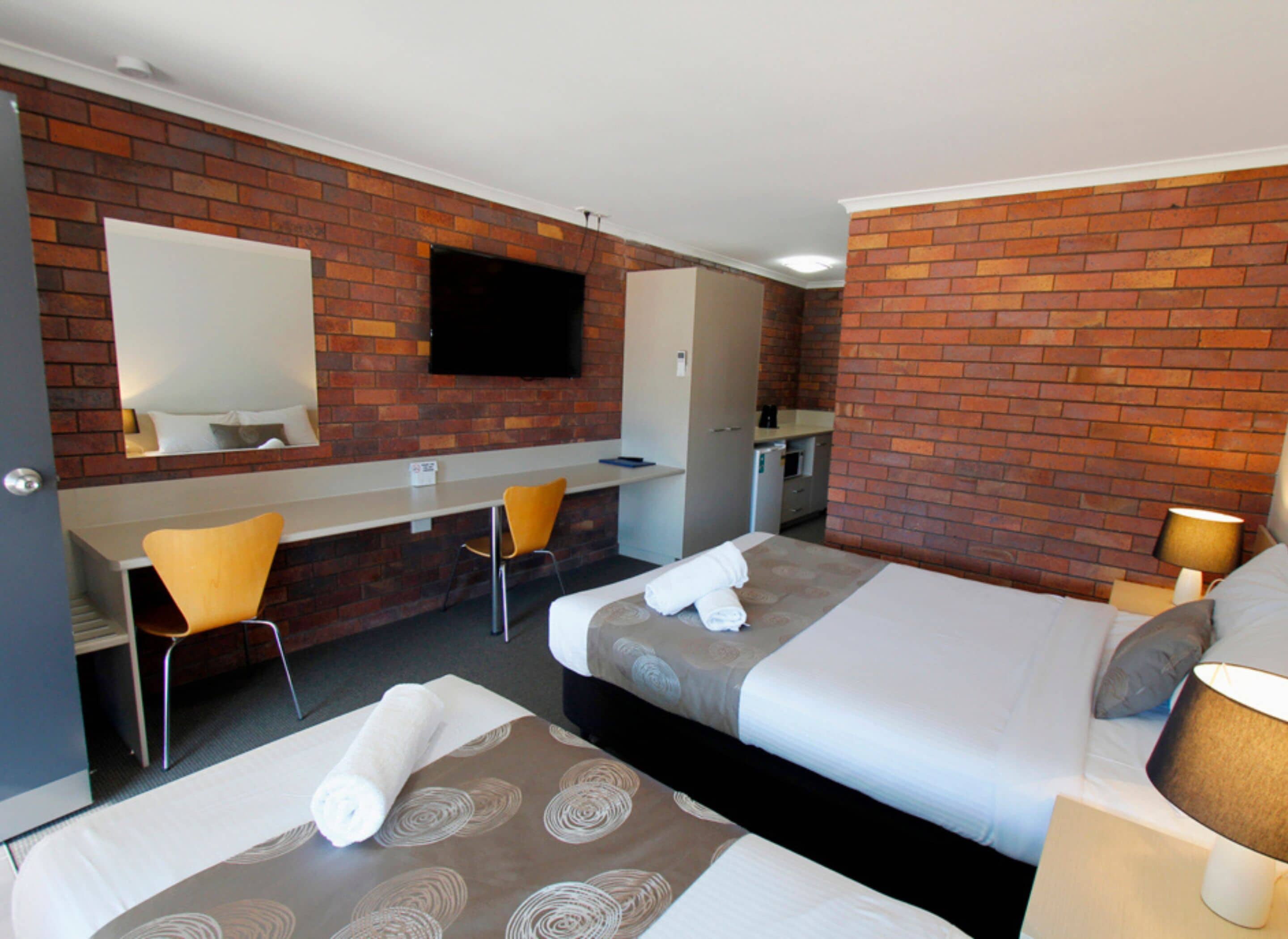 Habitación de hotel con dos camas, un escritorio, una silla, un televisor y una pared de ladrillo.