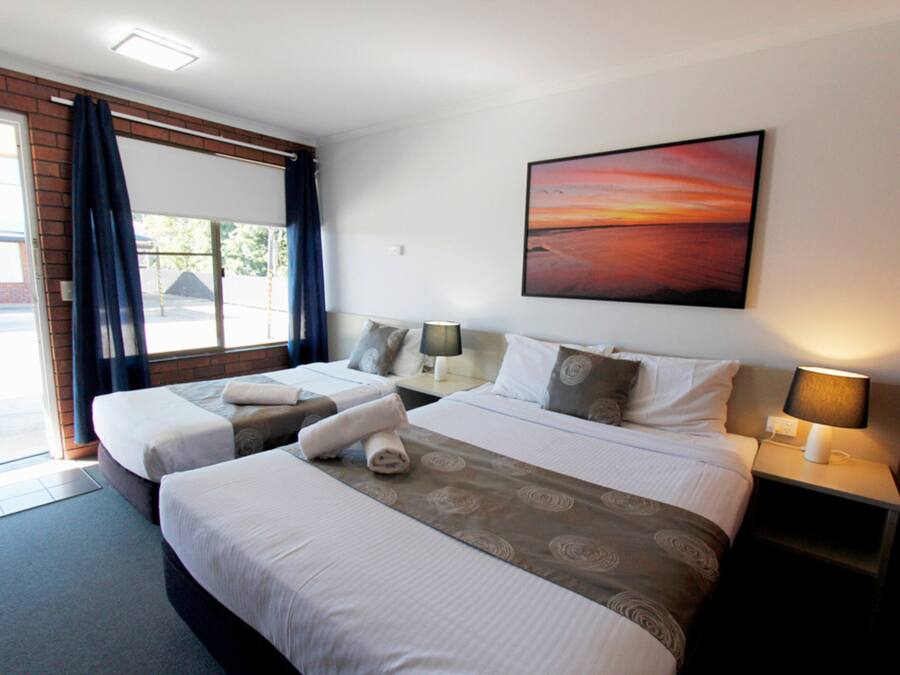 A hotel room with two beds, a large window with curtains, a painting on the wall, and two bedside lamps.