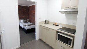 Une chambre d’hôtel compacte, dotée d’une kitchenette, d’un lit avec un mur de briques en arrière-plan et d’une petite salle de bain.