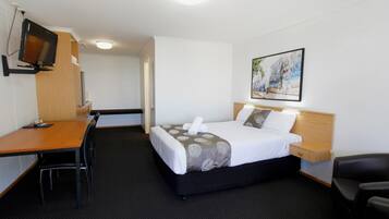 Una camera d'albergo con un letto, una scrivania, una sedia, una televisione e un quadro appeso al muro.