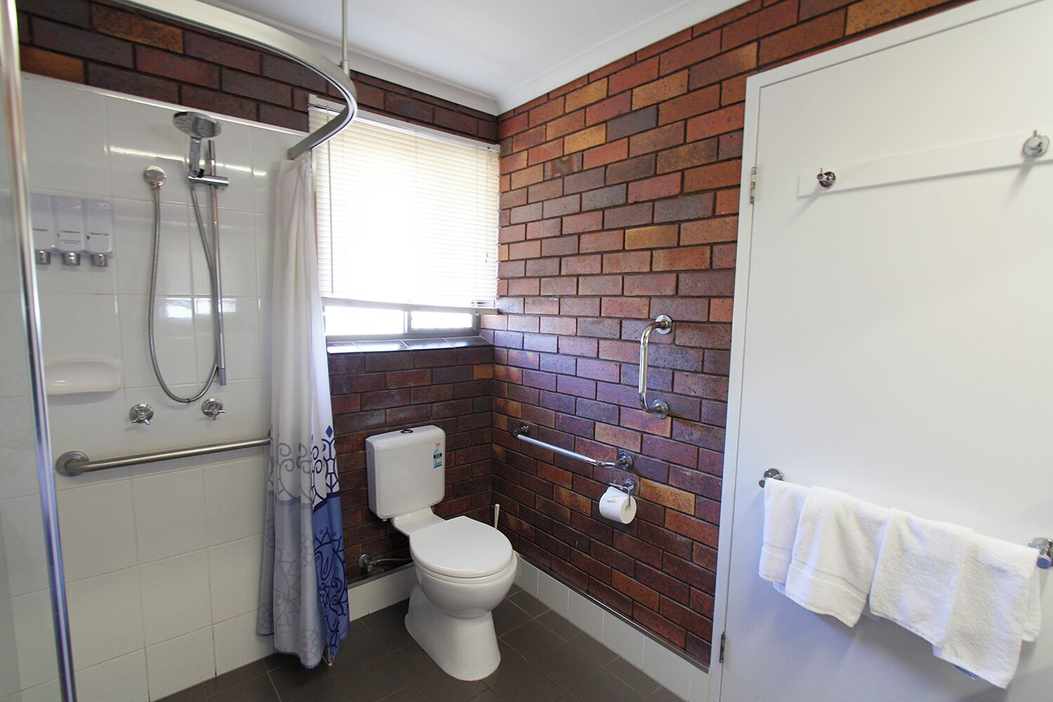 A bathroom with a shower, toilet, and a towel rack.