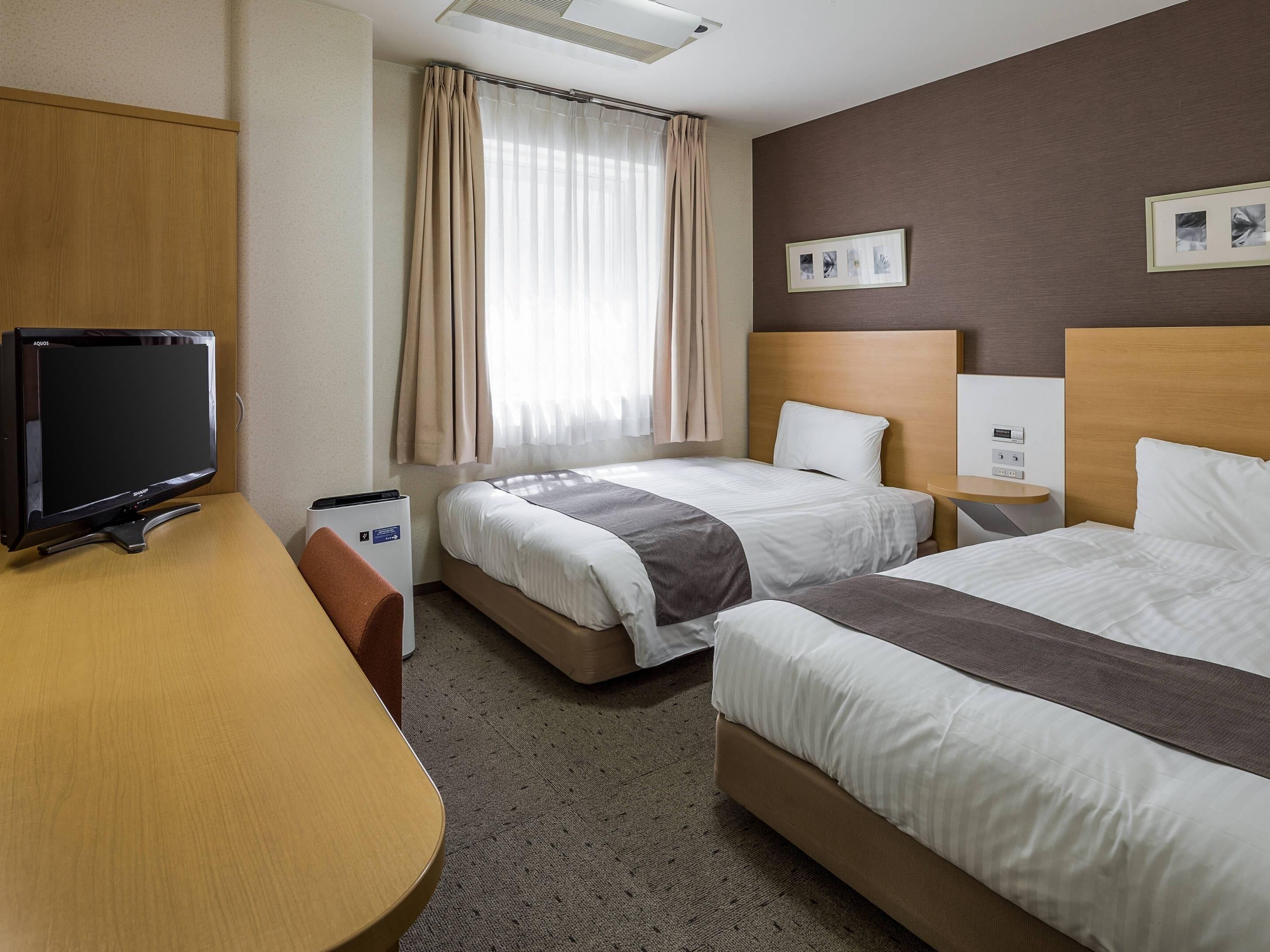 Habitación de hotel con dos camas, un escritorio, un televisor y una ventana con cortinas.