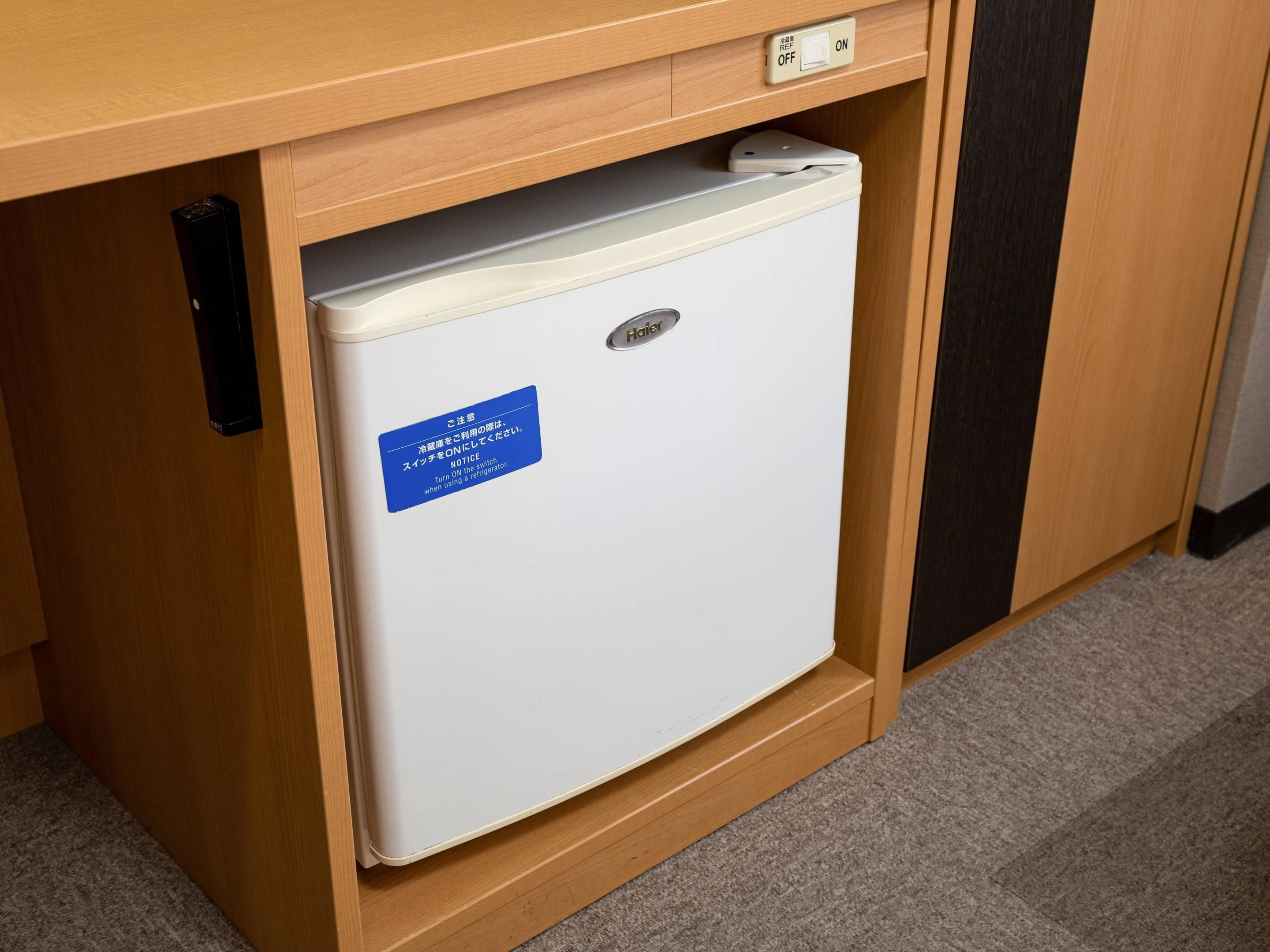 A compact white refrigerator with a blue label under a wooden counter, featuring a power switch and a control panel.