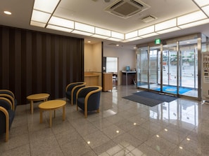 Un vestíbulo de hotel con asientos, un mostrador de recepción y una entrada con puerta de vidrio.
