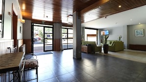 Un vestíbulo espacioso con techo de madera, una zona de recepción, un sofá verde y un televisor en la pared.