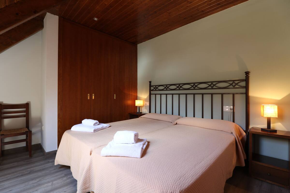Una cama bien tendida con cabecera, un armario de madera, una mesita de noche con lámpara y una silla.