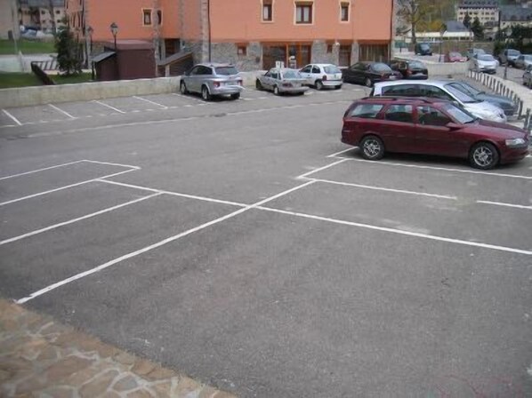 Un estacionamiento con varios coches, incluyendo una minivan roja, y un edificio de paredes naranjas al fondo.