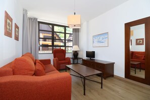 A living room with a sofa, armchair, coffee table, TV, and a large window with a view of buildings.