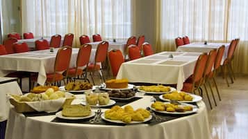 A banquet hall with multiple round tables covered with white tablecloths, red chairs, and a variety of food items displayed on the tables.