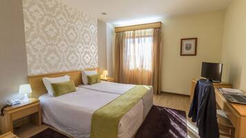 A hotel room with two beds, a desk with a computer, a TV, and a window with curtains.