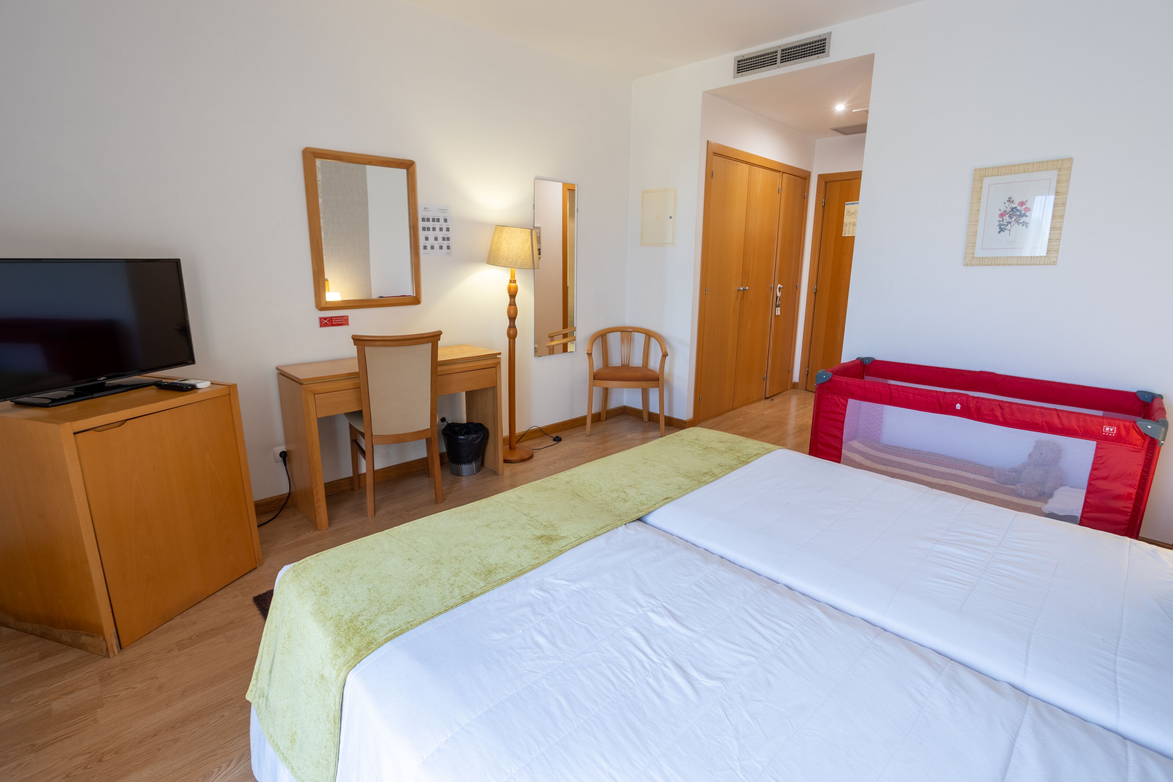 A hotel room with a bed, a desk, a chair, a television, and a red headboard.
