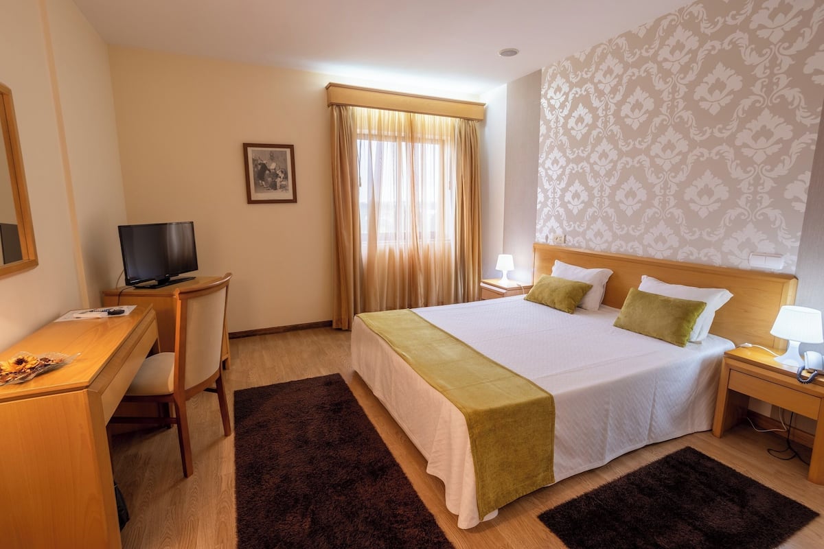 Ein Hotelzimmer mit einem Bett, einem Schreibtisch mit Fernseher, einer Lampe und einem Telefon.