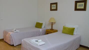 Two single beds with white bedding and green pillows, a wooden nightstand with a lamp, and a framed picture on the wall.