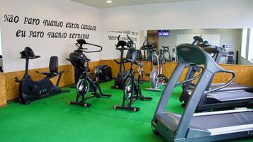 Uma academia com diversos equipamentos de cardio, carpete verde e frases motivacionais na parede.