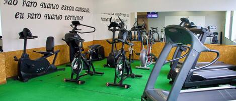 A gym with various cardio machines, a green carpet, and motivational wall text.
