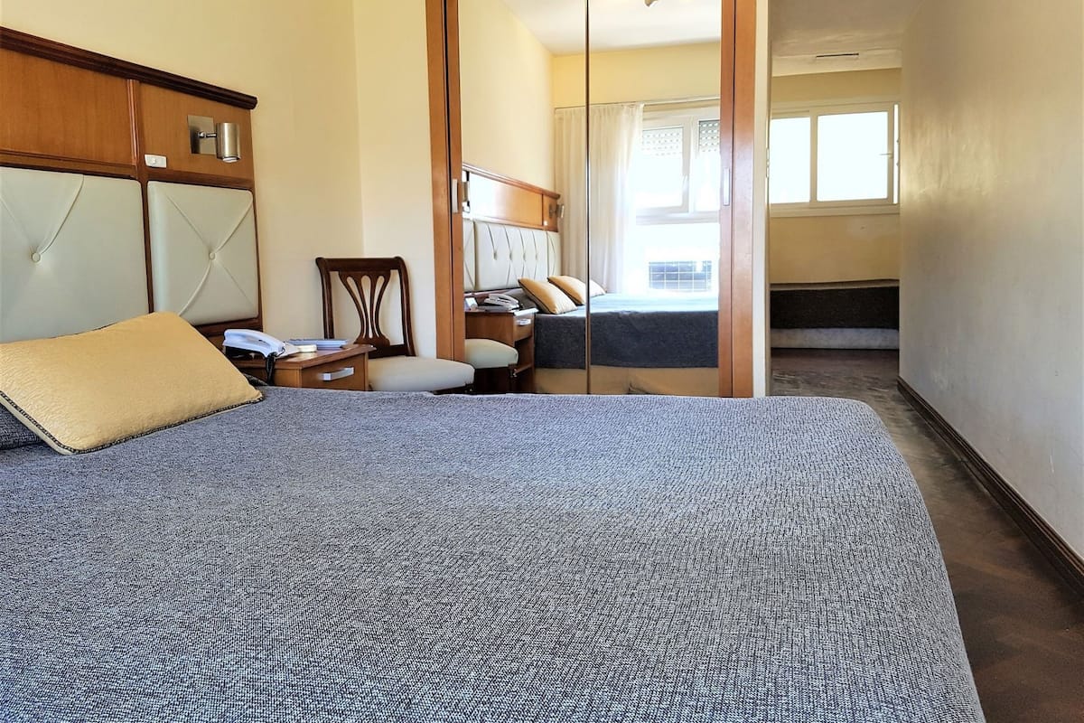 A bedroom with a bed, a desk, a chair, and a mirror.