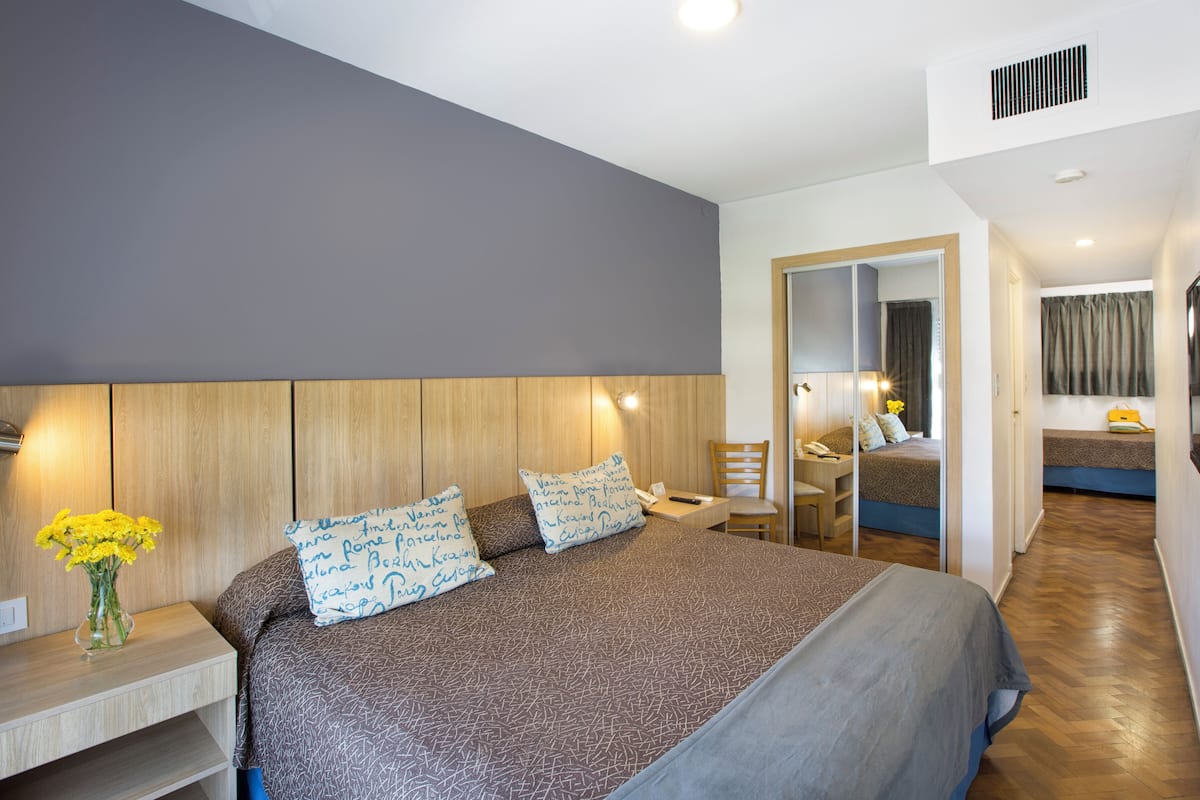 A modern hotel room with a large bed, a desk, and a mirror.