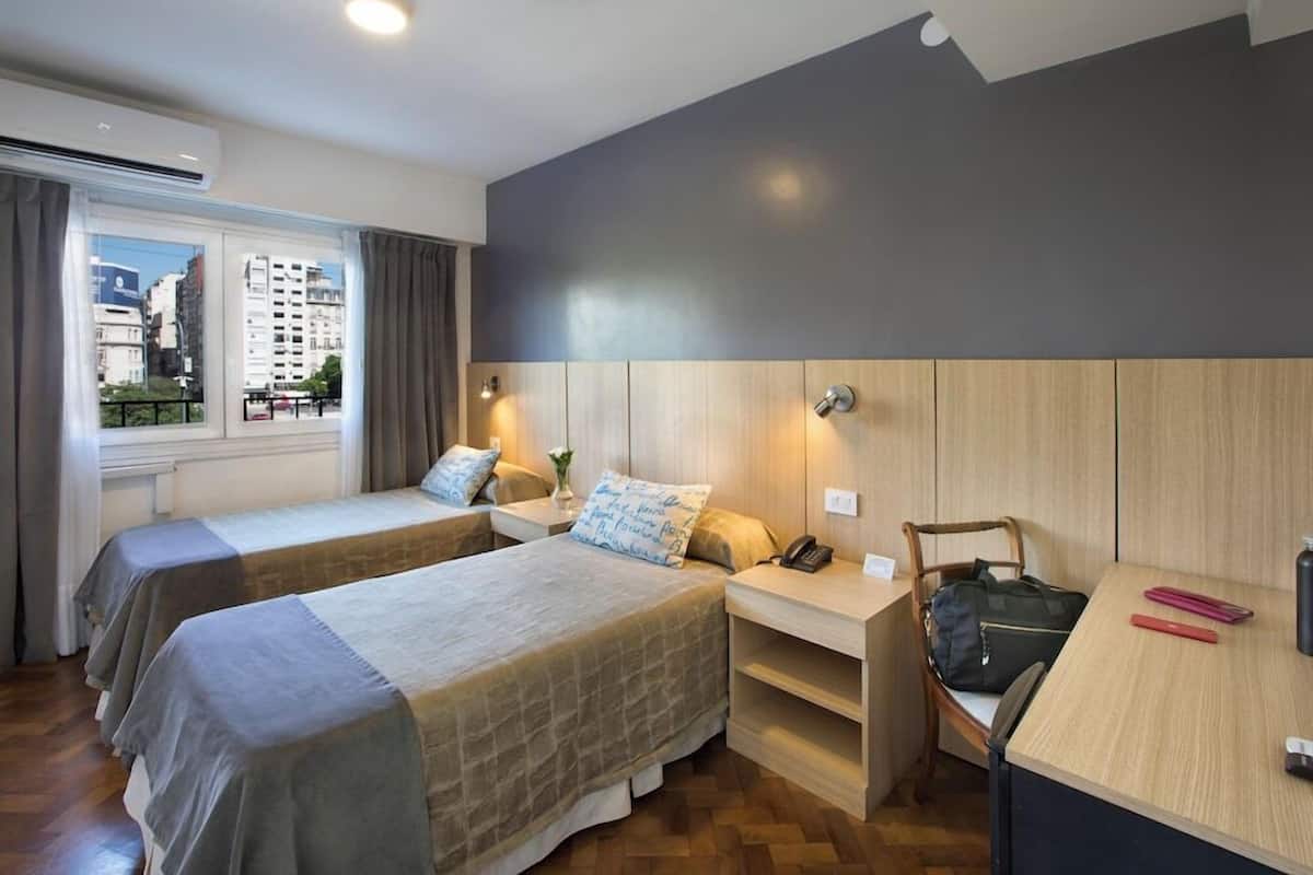 A hotel room with two beds, a desk, a chair, a phone, and a window with curtains.