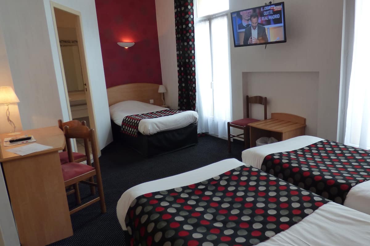 Une chambre d’hôtel avec deux lits, un bureau, une chaise, une télévision et une fenêtre avec des rideaux.