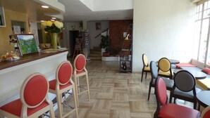 A restaurant interior with a wooden herringbone floor, red and yellow chairs, and a counter with a flower vase.