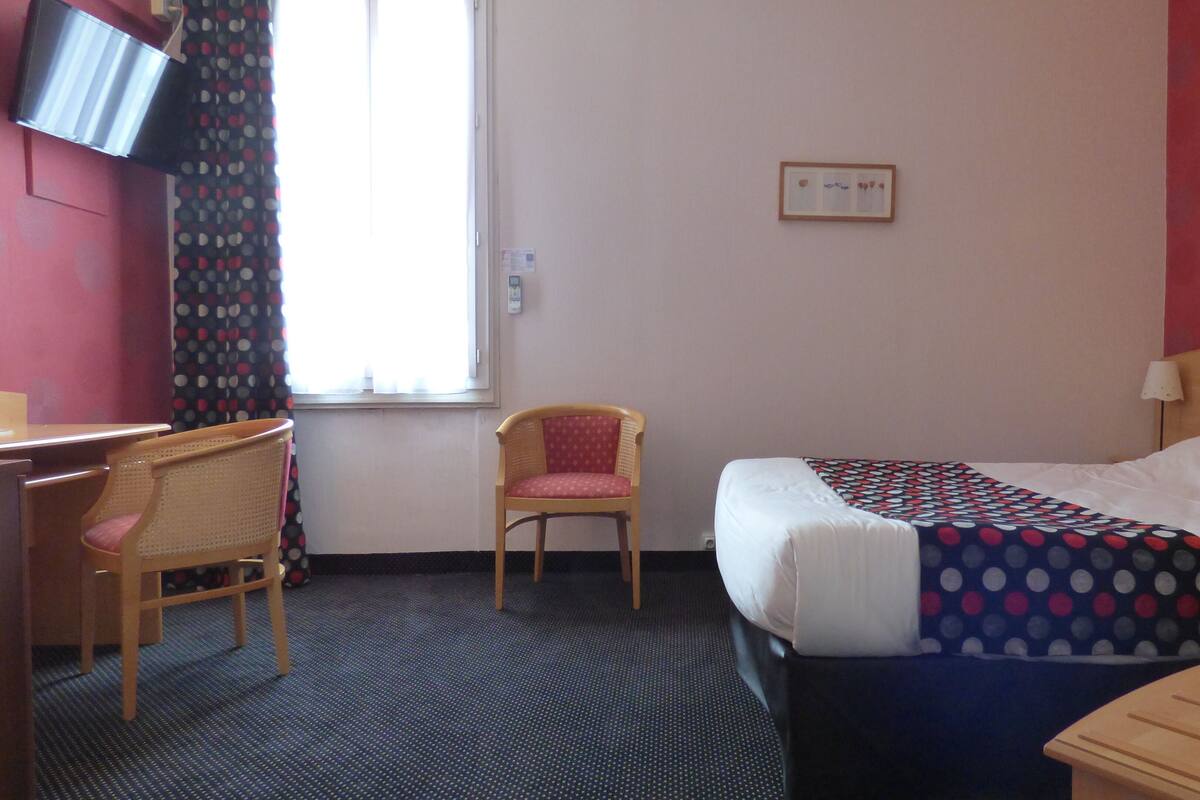 Une chambre d’hôtel avec un lit, une chaise, un bureau et un téléviseur fixé au mur.