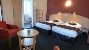 A hotel room with two beds, a small table, a chair, and a bookshelf.