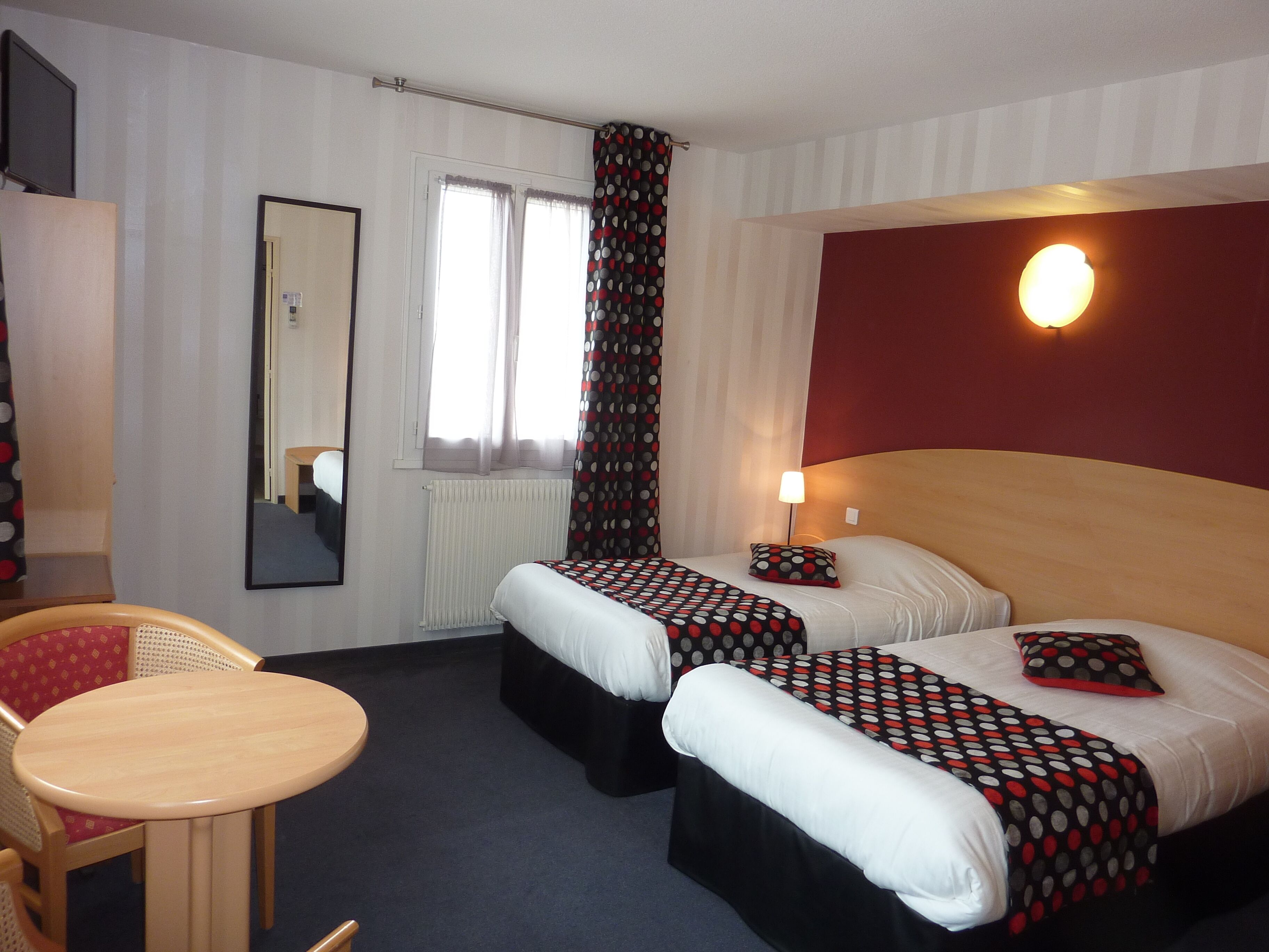 Une chambre d’hôtel avec deux lits, une petite table, une chaise, un miroir et une fenêtre avec des rideaux.