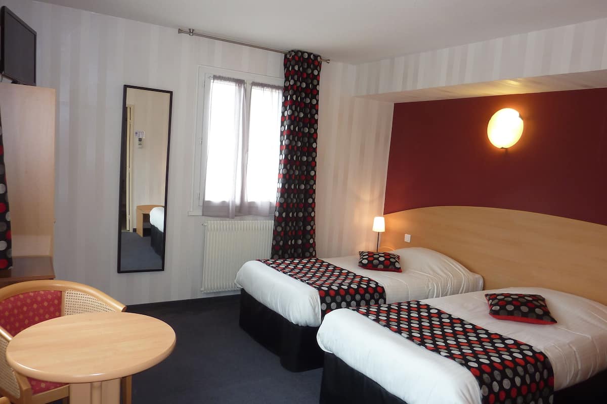 Une chambre d’hôtel avec deux lits, une petite table, une chaise, un miroir et une fenêtre avec des rideaux.