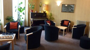 A living room with a piano, several chairs, a table with a chess set, and potted plants.