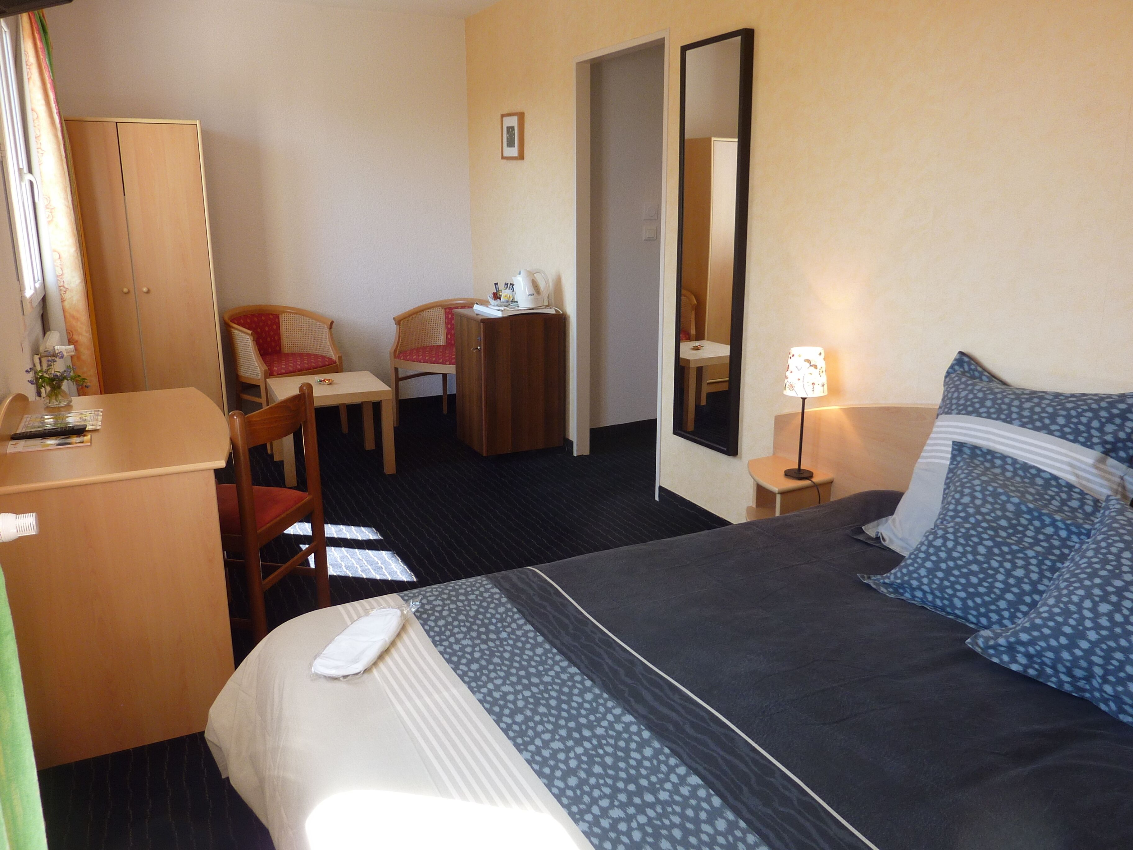 Une chambre d’hôtel comprenant un lit, un bureau, une chaise, une armoire, un miroir et une table de chevet avec une lampe.