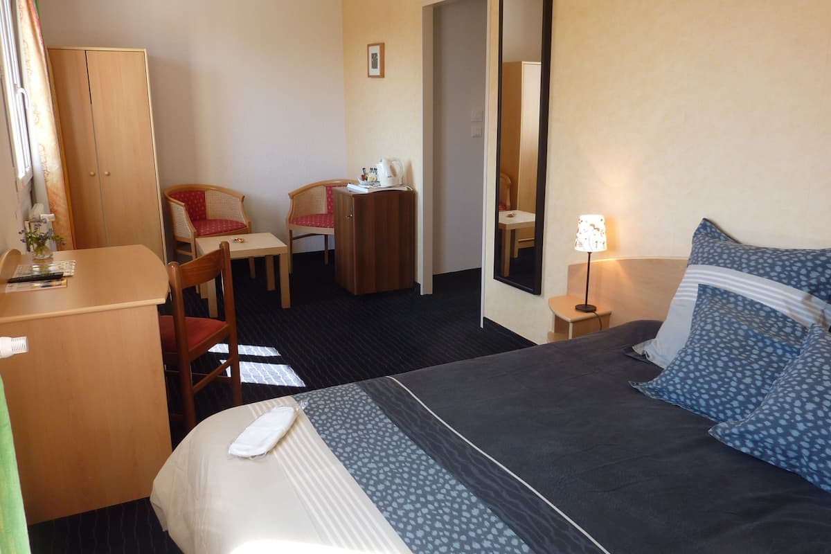 Une chambre d’hôtel comprenant un lit, un bureau, une chaise, une armoire, un miroir et une table de chevet avec une lampe.