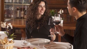 Una mesa de comedor dispuesta con platos, vasos y una variedad de alimentos, incluyendo queso y embutidos.
