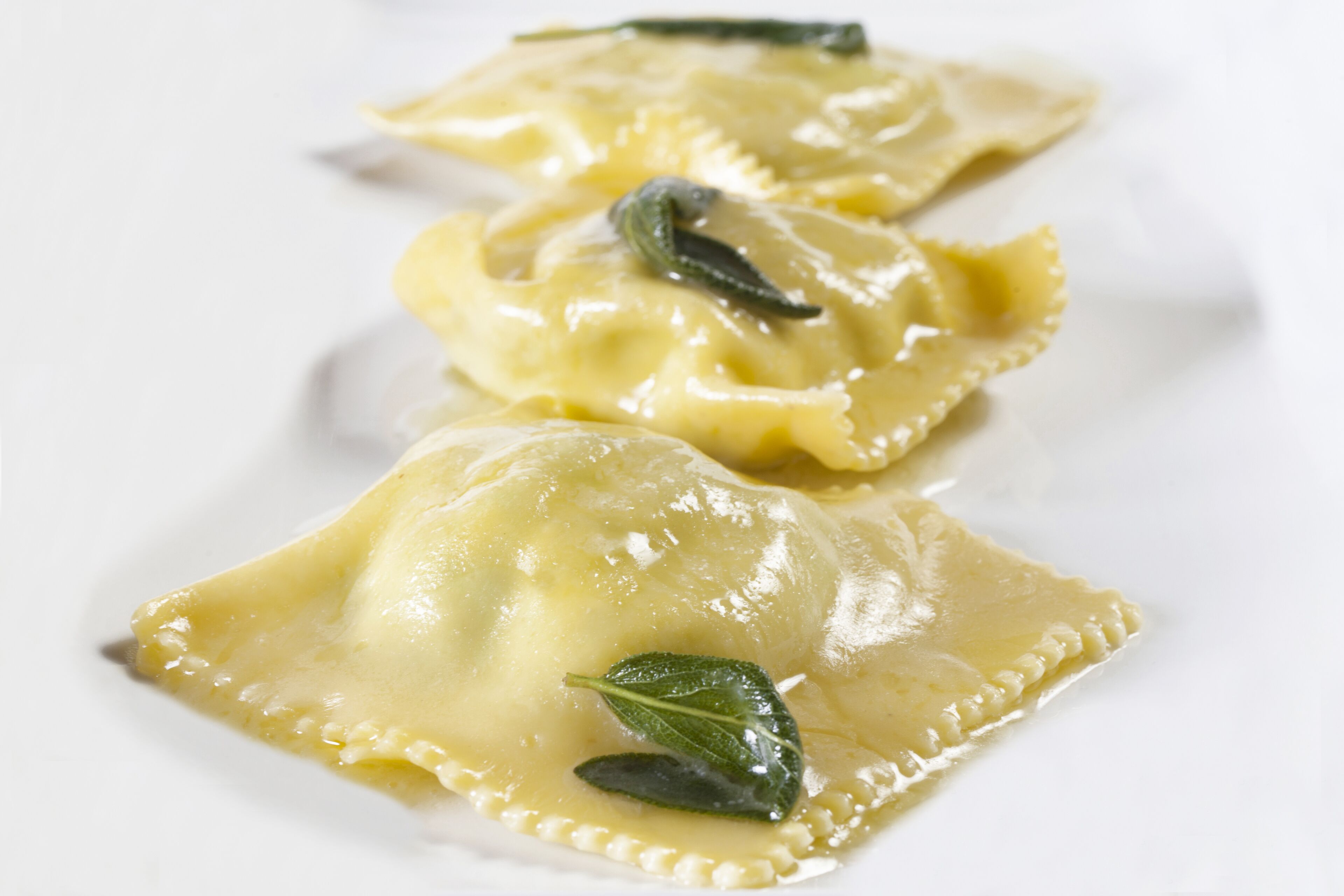 Three ravioli on a white plate with sage leaves.