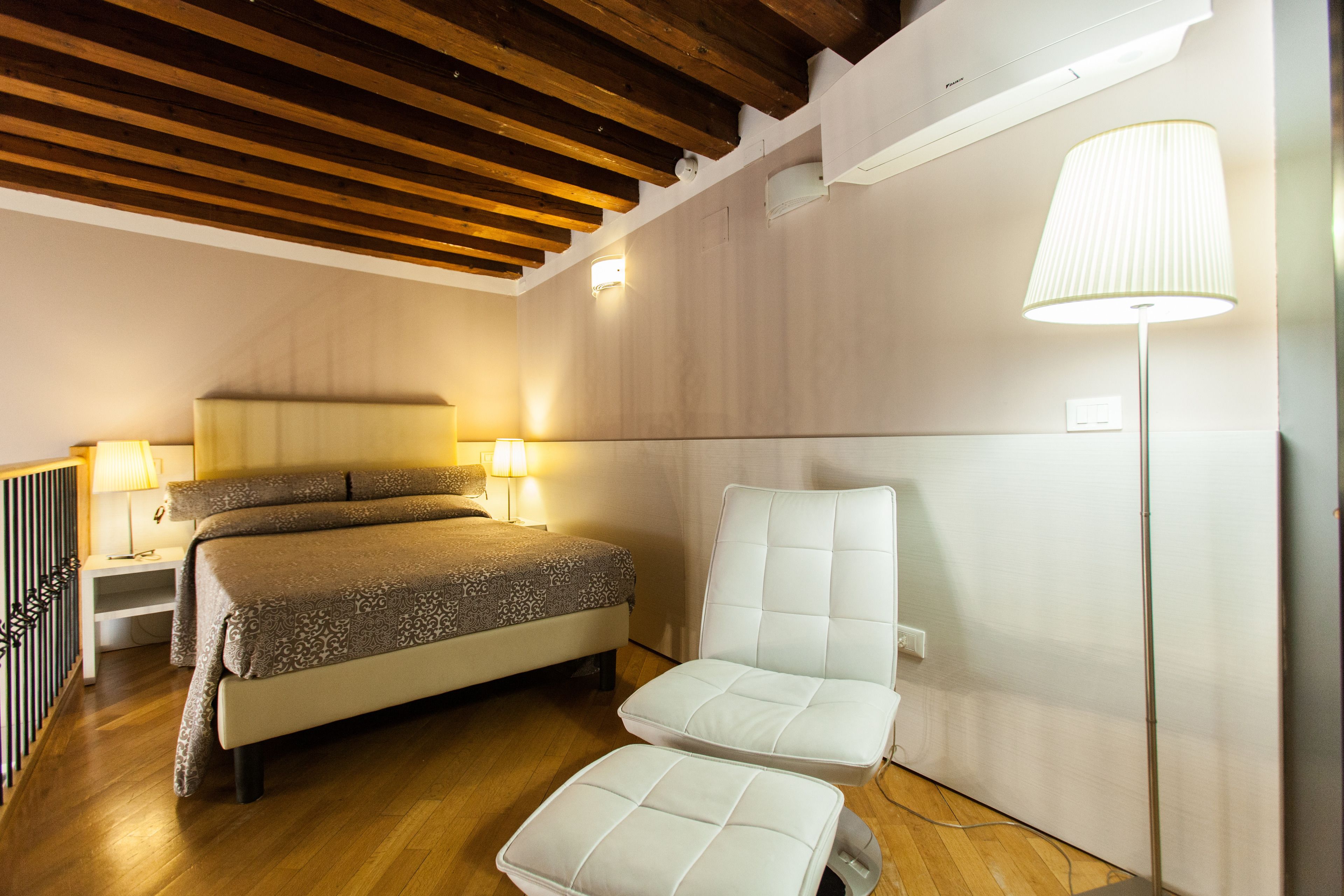 Un dormitorio con cama, lámparas de noche, una silla y una lámpara de pie.