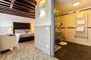 A modern hotel room with a bed, bedside table, lamp, and a shower area.