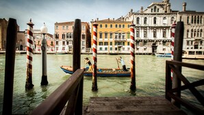 A wooden dock leading to a canal with a boat and buildings in the background. - Foresteria Levi (Venice)