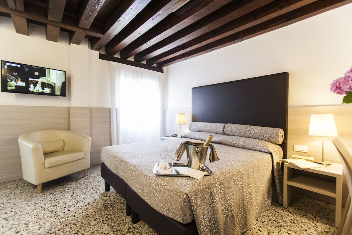 Una habitación de hotel con una cama, una silla, un televisor y una mesita de noche con lámpara.