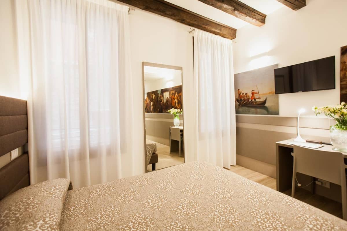 Un dormitorio con cama, escritorio, espejo y un cuadro en la pared.