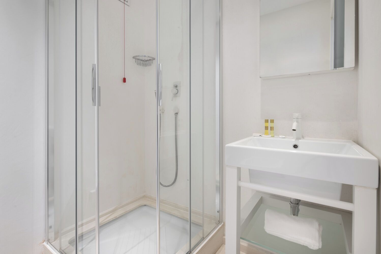 Un bany modern amb dutxa de vidre, un lavabo blanc i un mirall a sobre.