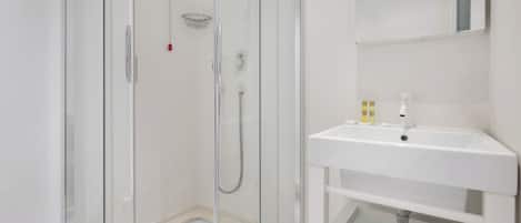 Un bany modern amb dutxa de vidre, un lavabo blanc i un mirall a sobre.