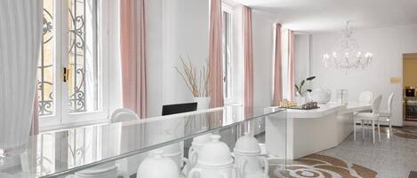 Une chambre d’hôtel moderne avec une cloison en verre, un comptoir d’accueil blanc et un lustre.