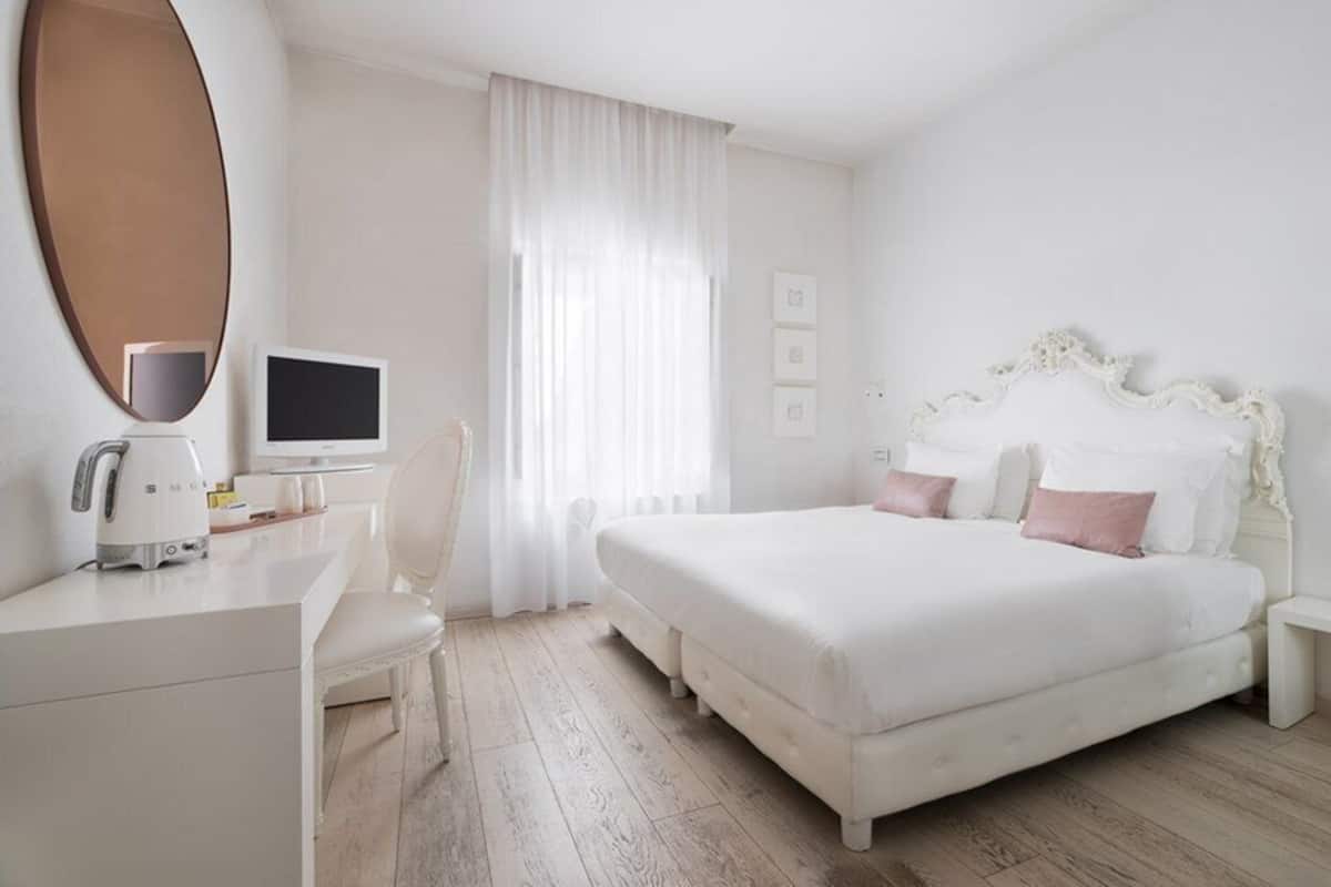 A hotel room with a large bed, a desk with a computer, a chair, and a large mirror.