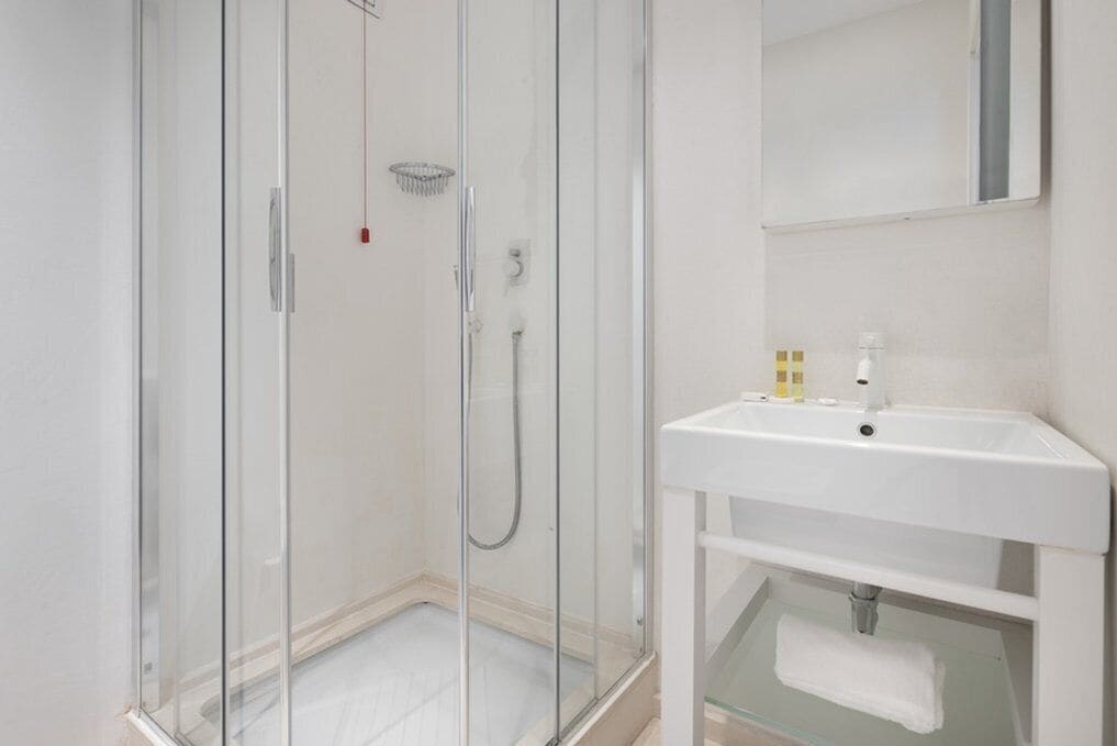 A modern bathroom with a glass-enclosed shower, a white sink, and a mirror above it.