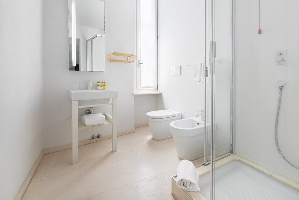 Ein modernes Badezimmer mit einer Duschkabine aus Glas, einem weißen Waschbecken mit Spiegel und einer Toilette.