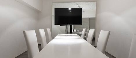 Un salón de conferencias con una larga mesa blanca, seis sillas blancas y un televisor de pantalla plana montado en la pared.