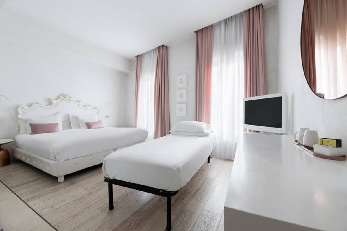 A hotel room with two beds, a TV, a bedside table, and a large window with curtains.