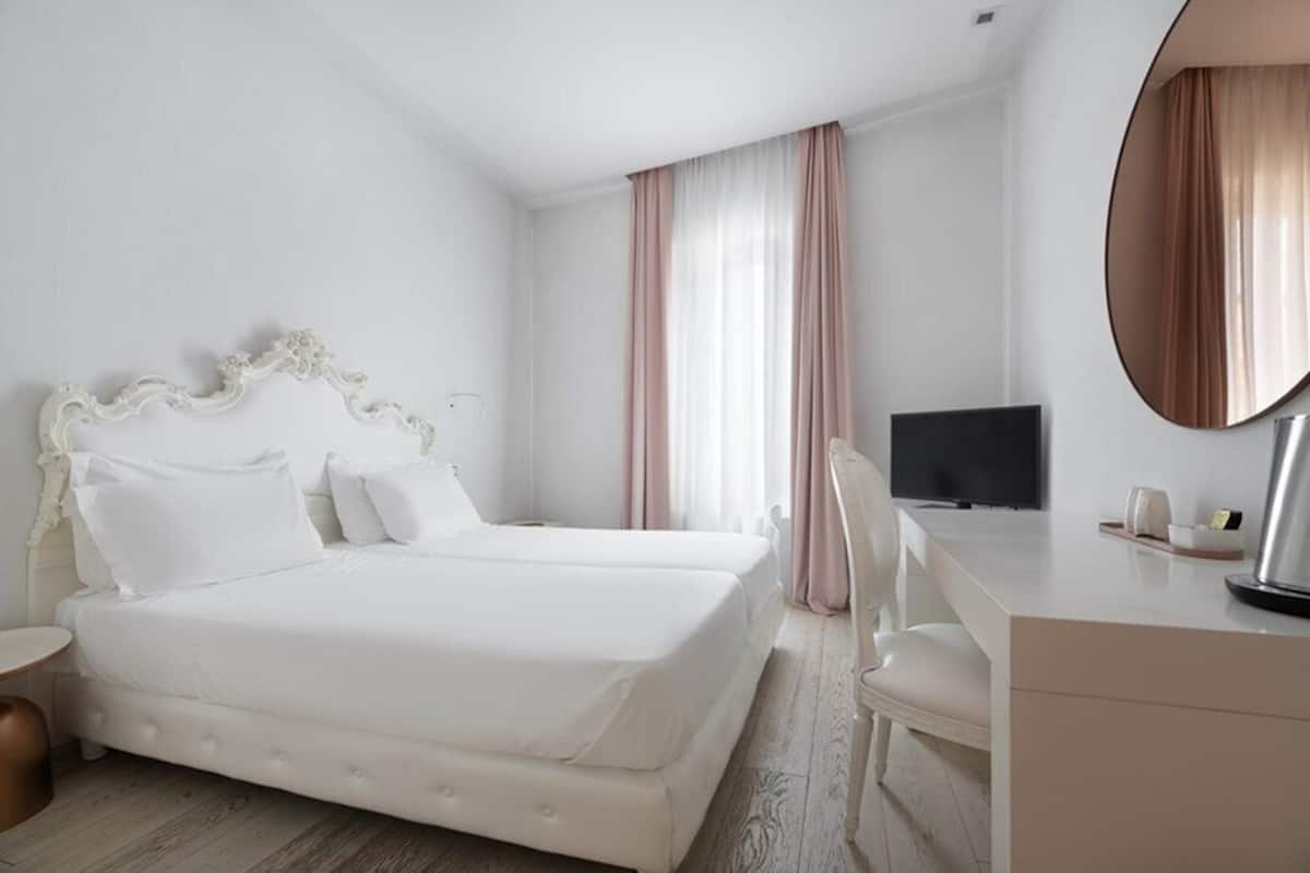 A hotel room with a double bed, a desk with a chair, a television, and a large mirror.