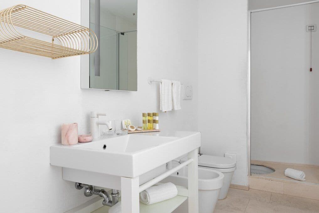 Ein modernes Badezimmer mit Waschbecken, Spiegel und Toilette in Weiß. An der Wand ist ein Handtuchhalter angebracht, im Hintergrund ist eine Duschkabine erkennbar.