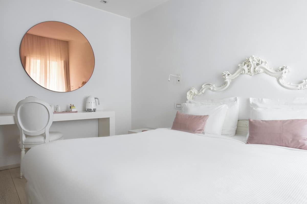 A hotel room with a large bed, a round mirror, a white desk, and a decorative headboard.